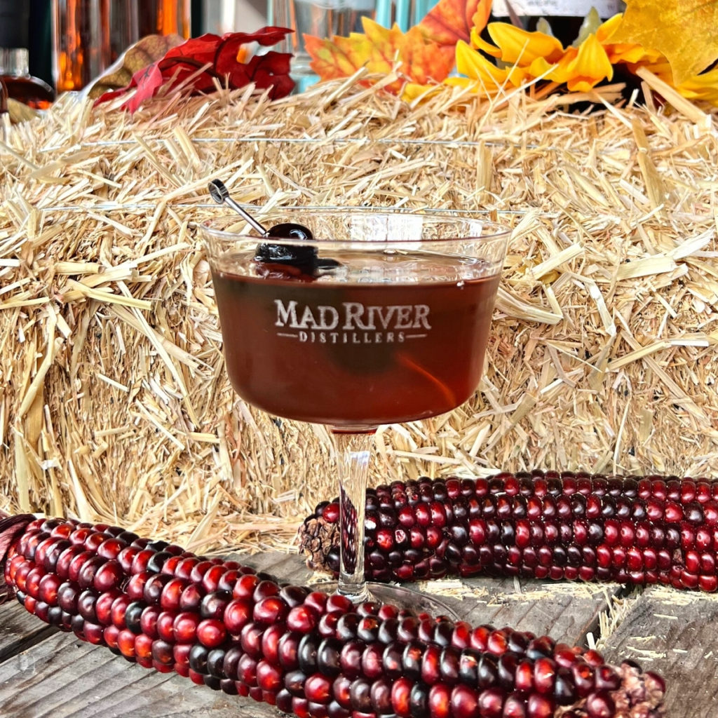 Rye Manhattan on a table in front of straw and corn