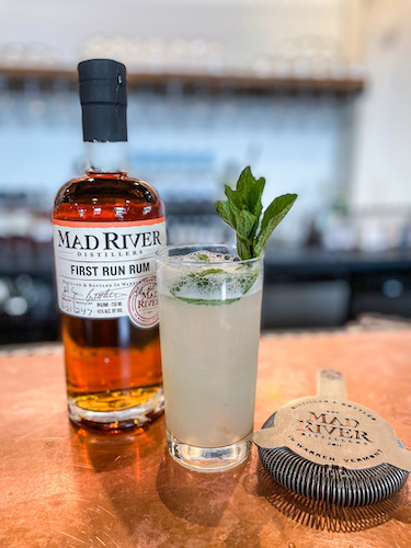 Bottle of First Run Rum, a strainer and cocktail on a bar