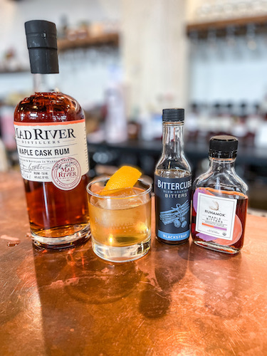 Bottle of Maple Cask Rum, bitters and a cocktail on a bar