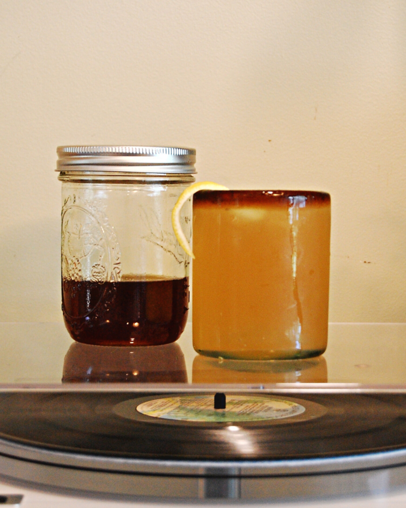 Ginger Drop cocktail on a table next to a jar of ginger honey syrup