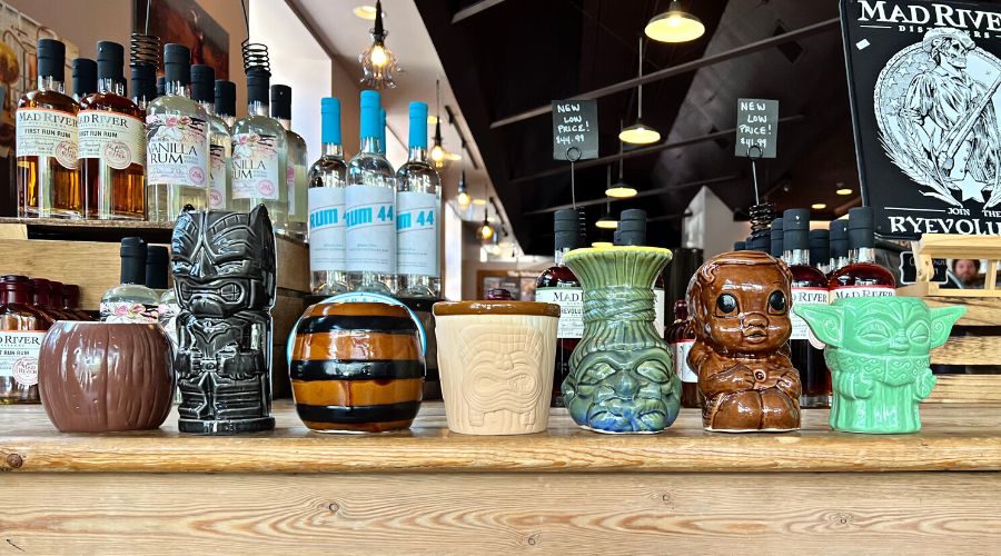A line of tiki mugs appear on a table