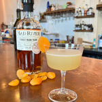 Apricot Blossom cocktail on the bar at Mad River Distillers with a bottle of First Run Rum and dried apricots