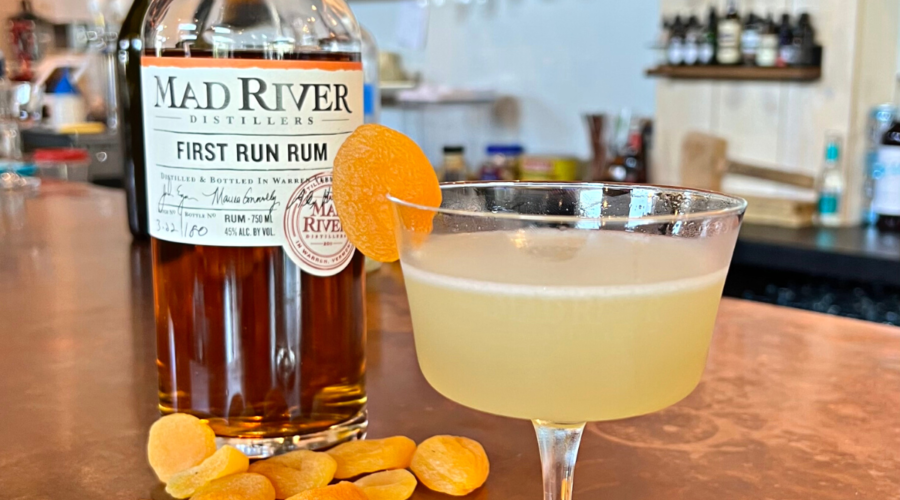 Apricot Blossom cocktail on the bar at Mad River Distillers with a bottle of First Run Rum and dried apricots