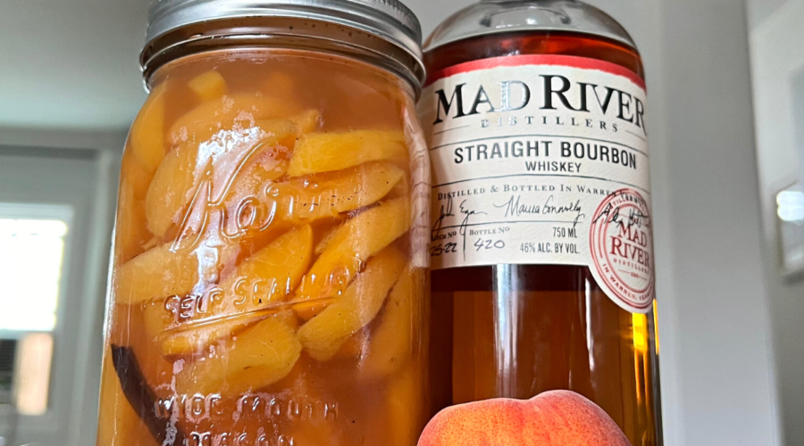 A jar of Straight-Bourbon poached peaches and a bottle of Bourbon on a counter